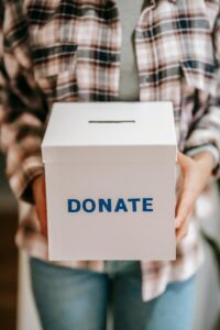 A person in a plaid shirt holding a white donate box.