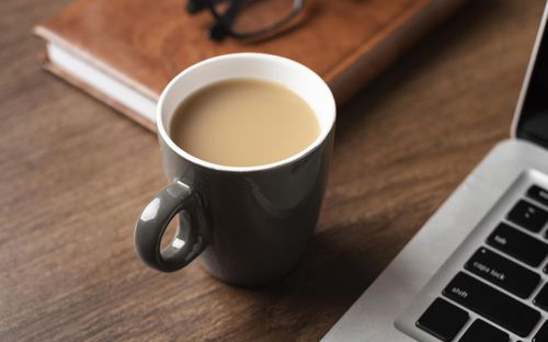 A cup of coffee next to a computer.