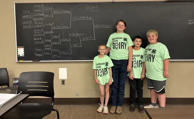 4 students standing against a chalk board wearing a Washtenaw Country Dairy Shirt