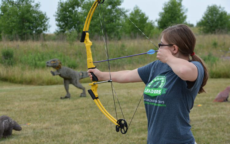 A girl holding a bow and pointing it at a target.